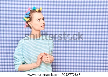 Portrait of thoughtful young woman without makeup with colorful hair curlers on head, looking melancholic and dreamy, standing over shower curtain background, with place for your text and design Royalty-Free Stock Photo #2052772868