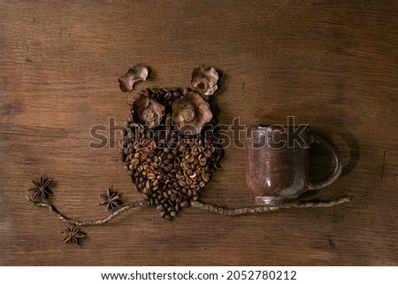 Owl shape from coffee beans and spices. Owl sit on the branch with coffee cup over wooden background. Funny mystery coffee concept
