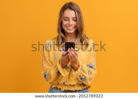 beautiful attractive smiling woman in yellow shirt holding using smartphone posing on yellow background isolated