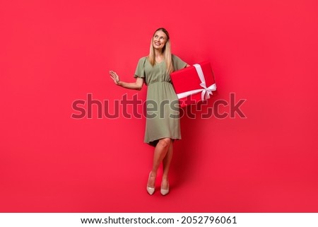 Photo of charming sweet young woman dressed green clothes holding big present box looking empty space isolated red color background