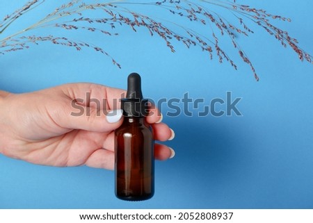 Beautiful groomed woman's hands with serum bottle on blue background. Pattern of beauty products packaging