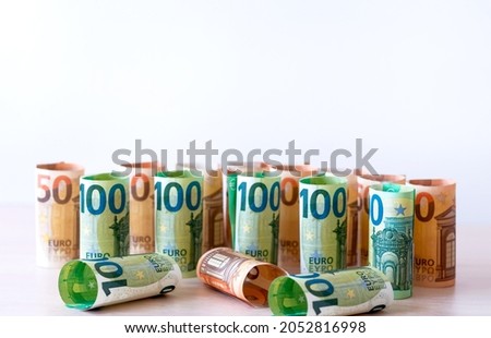 Many euro bills worth 100 and 50, folded into a roll one at a time, stand in a row. Free space