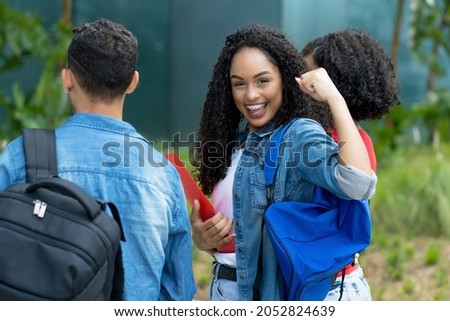 Cheering hispanic female student with braces and group of young adults at campus of university