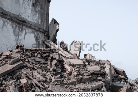 A ruined concrete building with a pile of rubble in the foreground against a gray sky background. Background. Royalty-Free Stock Photo #2052837878