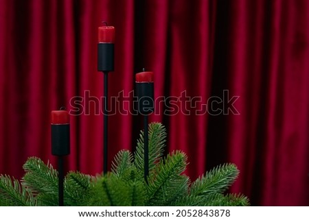 Red candles decorated with an artificial Christmas tree are on a background with burgundy curtains. High quality photo.