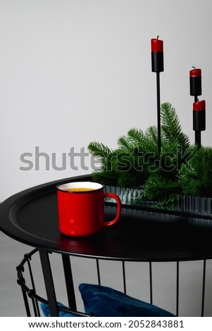 A red cup of coffee stands on the table next to red Christmas candles. High quality photo