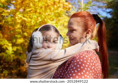 a red-haired happy woman with a little daughter in her arms in an autumn sunny park.