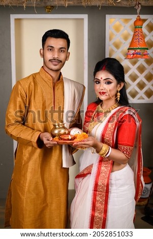 Portrait of Indian man dressed in kurta pyjama with beautiful Indian woman wearing traditional Indian saree, gold jewellery and bangles, holding plate of religious offering. Royalty-Free Stock Photo #2052851033