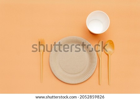 Recyclable fork, spoon, knife, plate and cup on a beige background. Kitchen utensils. Top view. Minimalist Style. Copy space.