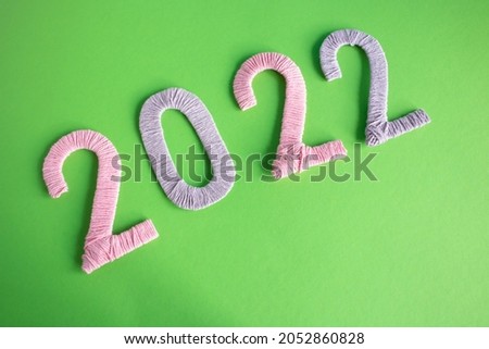 The numbers 2022, made of pink and lilac threads, lie on a green background. The concept of the New Year.