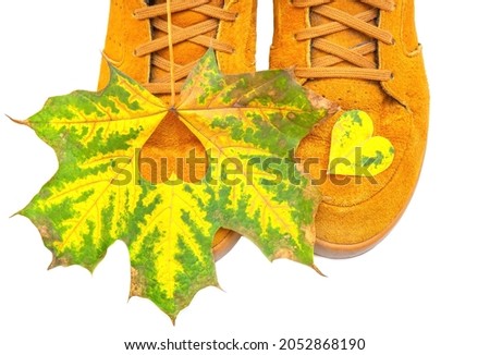 Maple leaf with a cut out heart lies on orange sneakers isolated on white
