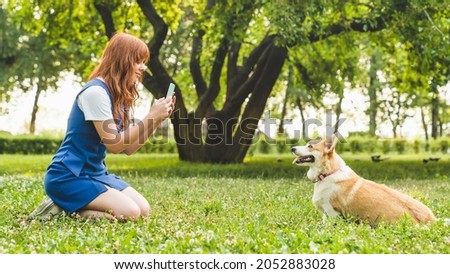 Caucasian young woman teenager girl student taking a photo of her dog welsh corgi while walking taking care of a pet together in park garden forest.