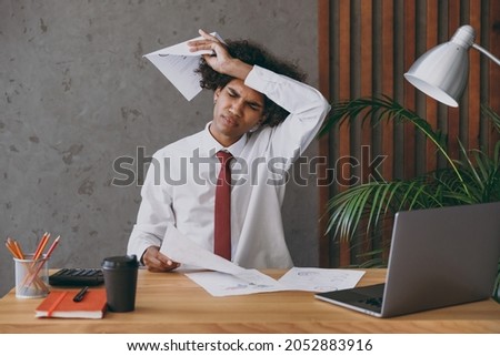 Young african american employee business man in classic shirt tie hold paper account documents put hand on head forehead sit work at white office desk with pc laptop inside Achievement career concept