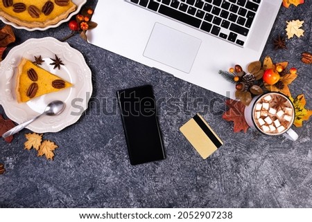 Workspace with laptop and Hot chocolate and homemade pumpkin pie with cinnamon and pecan nuts. Online shopping with phone and credit card