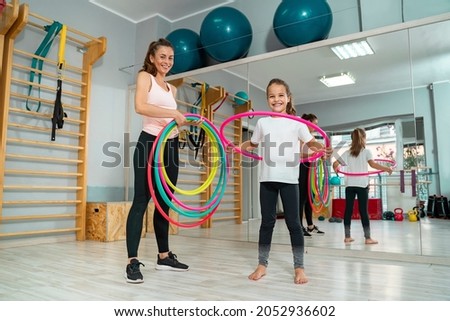 Little girl with hoola hoop in the gym with her pe teacher or trainer, kids health and activity 