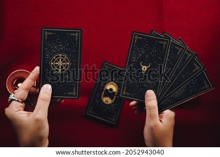 Fortune teller woman and a black tarot cards over red table background and candles. Royalty-Free Stock Photo #2052943040