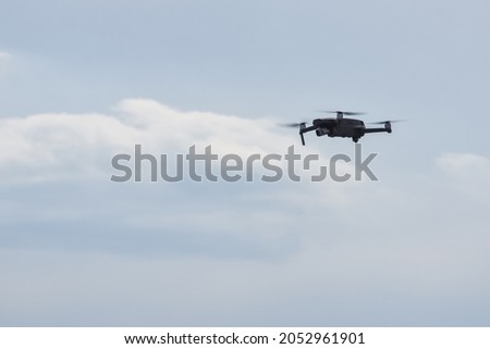 small drone quadcopter flies with a camera on a background of blue sky with clouds.