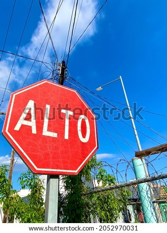 Stop sign against the blue sky and power lines in Cabo San Lucas, Mexico. Barbed wire and greenery in the background. Bright colors make this an interesting statement.