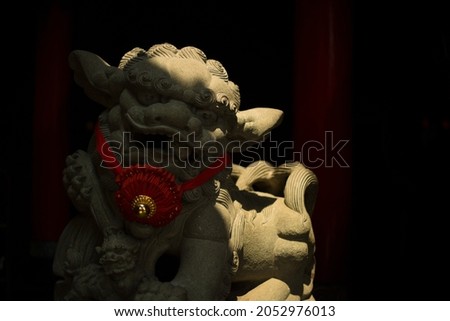 Stone Chinese guard lion with gold necklace with red band at one of the temples in the city of Jakarta.