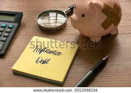 Selective focus of calculator, magnifying glass, piggy bank, pen and memo note written with Refinance Debt on wooden background.