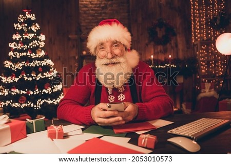 Photo of influencer santa claus sit workspace hold telephone blog post wear hat sweater in north pole office indoors