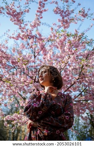 Portrait of a cute and beautiful woman girl in a dress in the garden in the middle of blooming sakura. spring and sun time. Blurred background and selected focus.