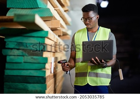 African American warehouse worker using laptop and scanning labels at lumber storage compartment. Royalty-Free Stock Photo #2053035785