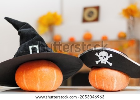 Halloween pumpkins with witches and pirate hats on the table against the background of a home rustic fireplace with autumn decorations.