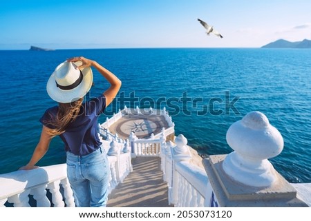 Carefree young tourist woman in sun hat enjoying sea view at Balcon del Mediterraneo in Benidorm, Spain. Summer vacation in Spain Royalty-Free Stock Photo #2053073120