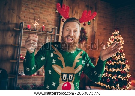 Photo of cheerful guy hold bengal fire stick enjoy atmosphere wear reindeer headband jumper decorated home indoors Royalty-Free Stock Photo #2053073978