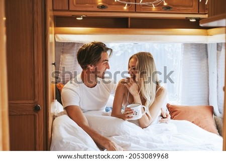 couple in love having fun together in bed in morning, young man and woman newlyweds hugging on cozy bed in trailer mobile home or recreational vehicle during family local travel Royalty-Free Stock Photo #2053089968