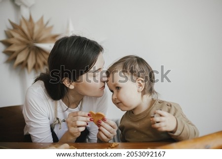 Cute daughter and mother making together christmas cookies on messy table. Adorable toddler girl helper with mom cutting dough for gingerbread cookies. Family preparations for xmas holidays
