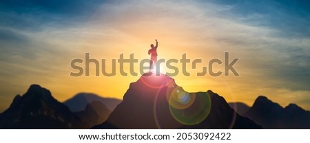 Silhouette of businessman celebrating raising arms on the top of mountain with over blue sky and sunlight.concept of leadership successful achievement with goal,growth,up,win and objective target. Royalty-Free Stock Photo #2053092422