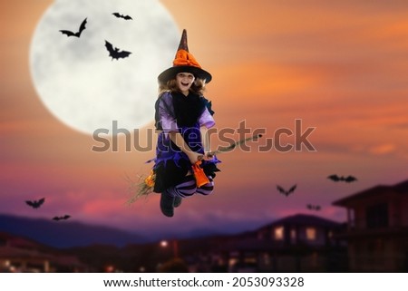 Little witch flying broom on Halloween night. Huge full moon and bats in the background. Kids trick or treat costume. Children have fun. Spooky and scary celebration. Kid dressed as evil ghost.