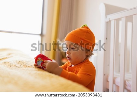 Cute caucasian infant baby Girl one year old in orange costume with pumpkin face at home. Happy Halloween concept