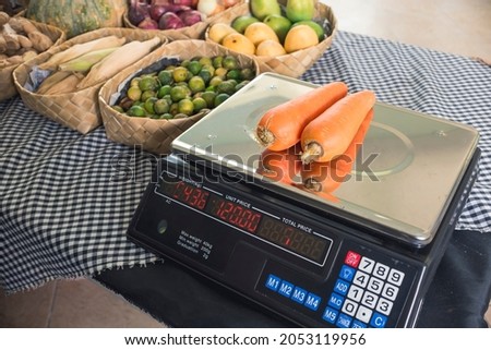 Two carrots are weighed on a digital scale. Equipment of a small outdoor stall at a public market.