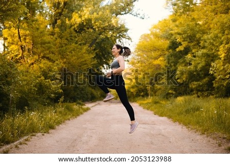 Dynamic photo of a woman jumping high while making some sport exercises in the forest park.