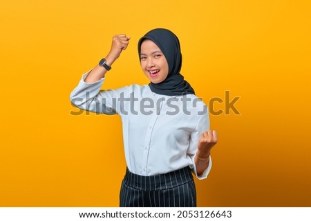 Portrait of excited beautiful Asian woman rejoicing celebrating luck on yellow background
