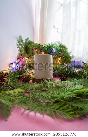 The composition features Christmas and New Year's products. white mug on old round wood with spruce leaf decoration