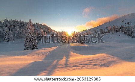Wide shot of a magical white winter sunset at Dobratsch Natural Park with fresh snow over footsteps and frost covered pine trees, Villach, Carinthia, Austria Royalty-Free Stock Photo #2053129385