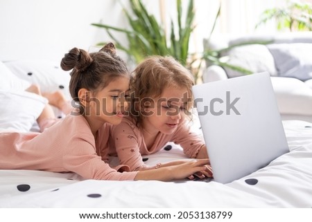 cute little kids girls in pajamas using laptop in bed at home. Kids using technology
