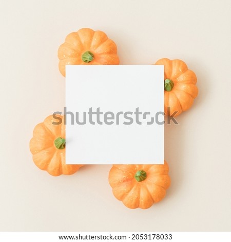 Creative autumn template with orange pumpkins and white paper card on pastel cream background. Minimal fall copy space.
