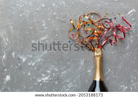 Creative flat lay composition with bottle of champagne and space for text on color background. Champagne bottle with colorful party streamers. holiday or christmas concept.