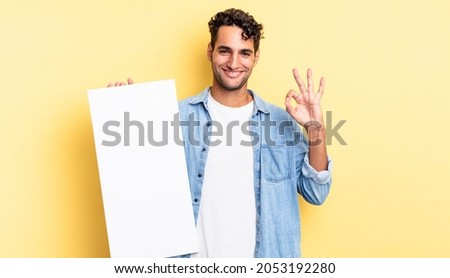 hispanic handsome man feeling happy, showing approval with okay gesture. empty canvas concept