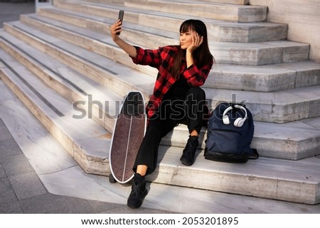 Portrait of young beautiful girl with skateboard. Happy smiling woman taking selfie photo	