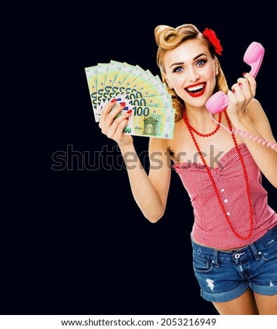 Photo of happy excited woman holding money euro cash banknotes, talking on phone, dressed in pin up style. Blond girl in retro fashion and vintage concept. Isolated over dark black background. Female 