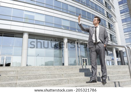 Full length of businessman taking self portrait on steps outside office