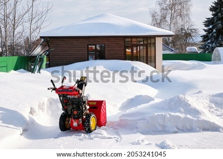 Red snowblower. Manual petrol snow blower. Pure snow. Drifts in the backyard of the house. Clear frosty day.