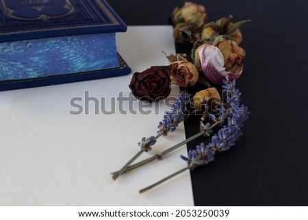 dried rosebuds and lavender branches on a textured sheet of paper with a colorful book behind on a black background. romantic letter