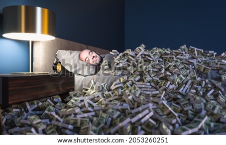 Smiling man sleeping in a bed covered with dollars money. wealth concept. Royalty-Free Stock Photo #2053260251
